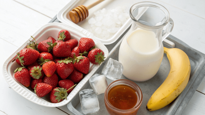 Fresh strawberries, milk, yogurt, honey, and ice displayed for smoothie preparation