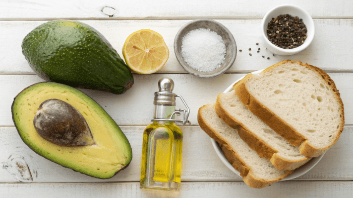 Ingredients for avocado toast including avocado, bread slices, lemon, and spices