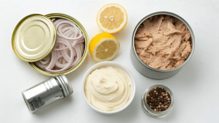 Ingredients for tuna salad including tuna can, mayo, onion, and vegetables